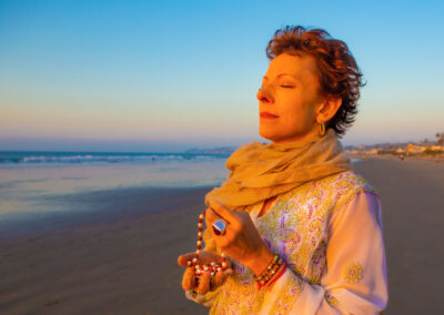 Jeanne on beach with eyes closed meditating and holding Mala beads